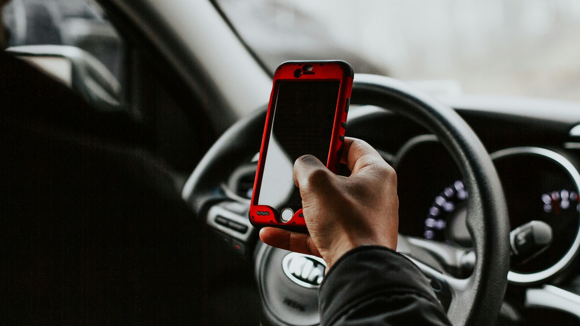 person holding red smartphone sitting in front of vehicle steering wheel