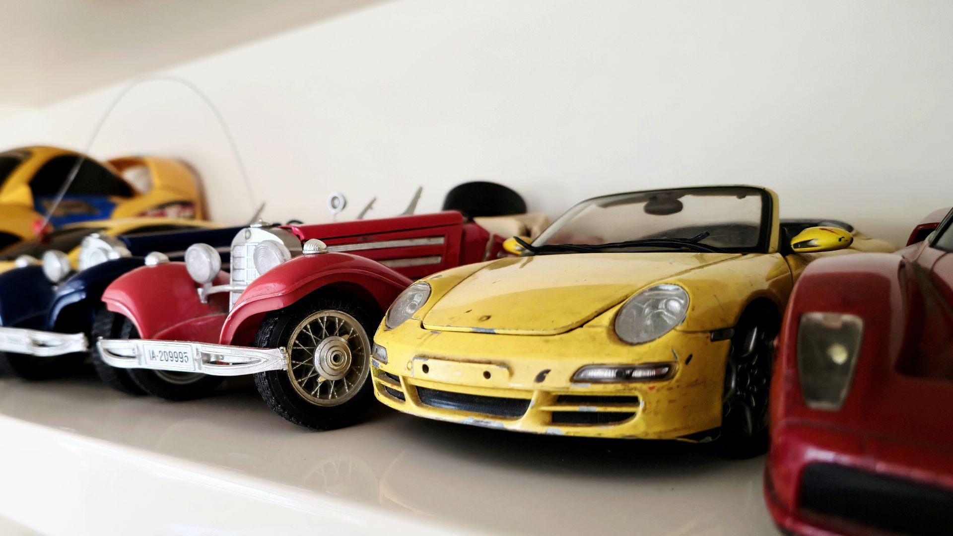 Toy cars are lined up on a white shelf.