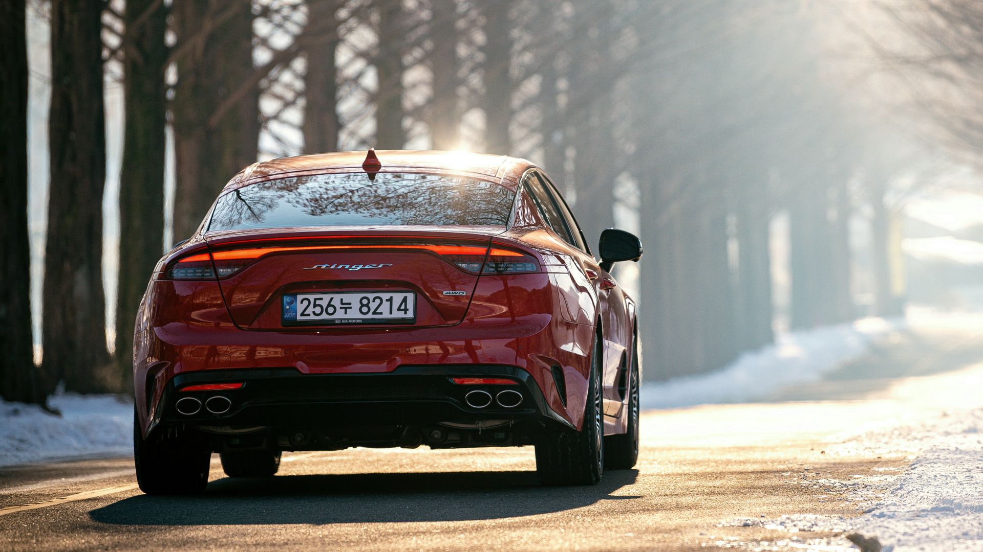 a red car driving on a road with snow on the side