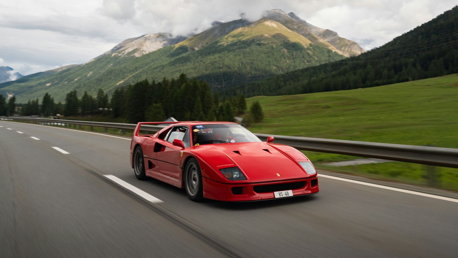 a red sports car driving on a road with mountains in the background