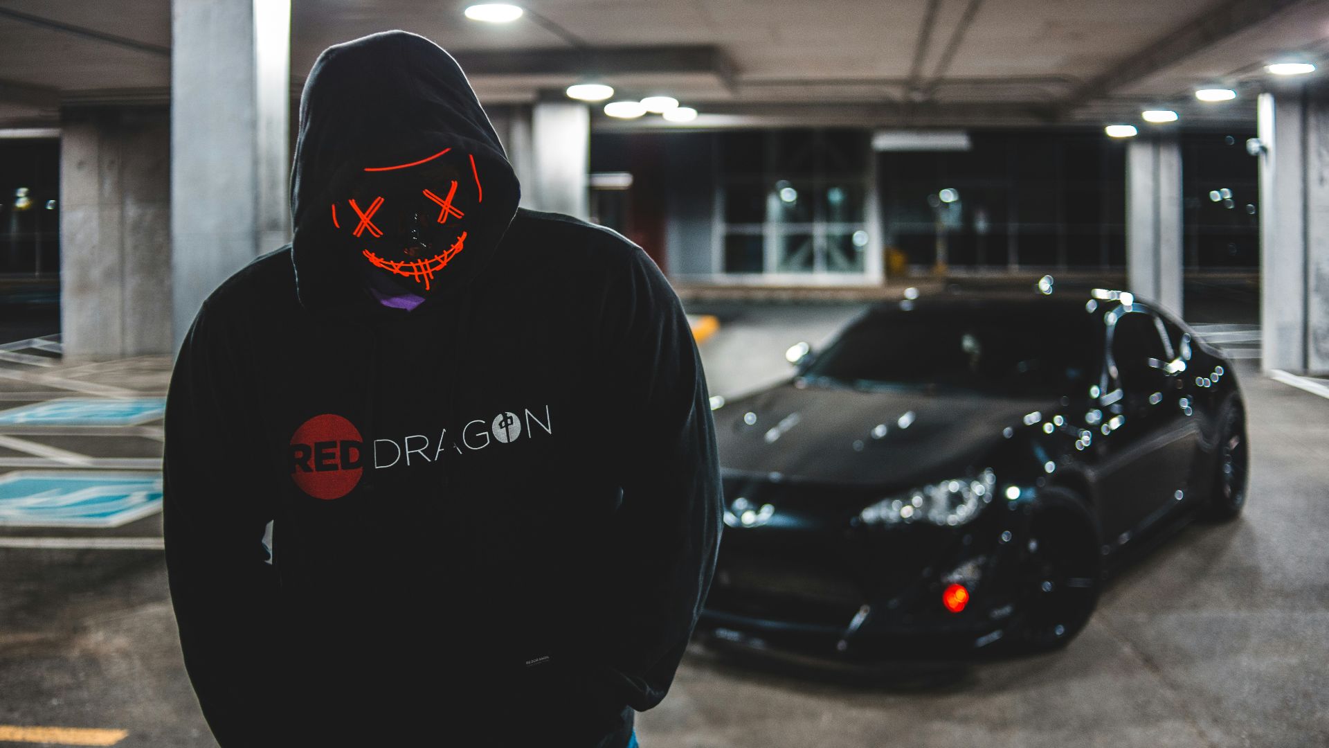 man in black hoodie standing beside black car