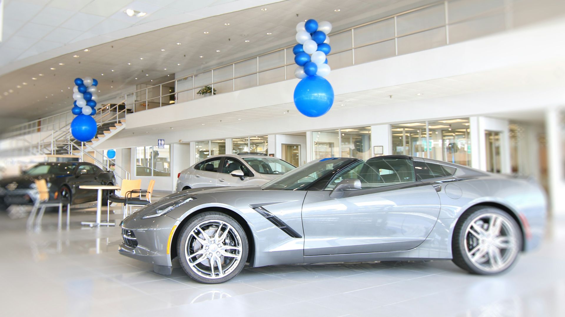 a silver sports car in a showroom with blue and white balloons