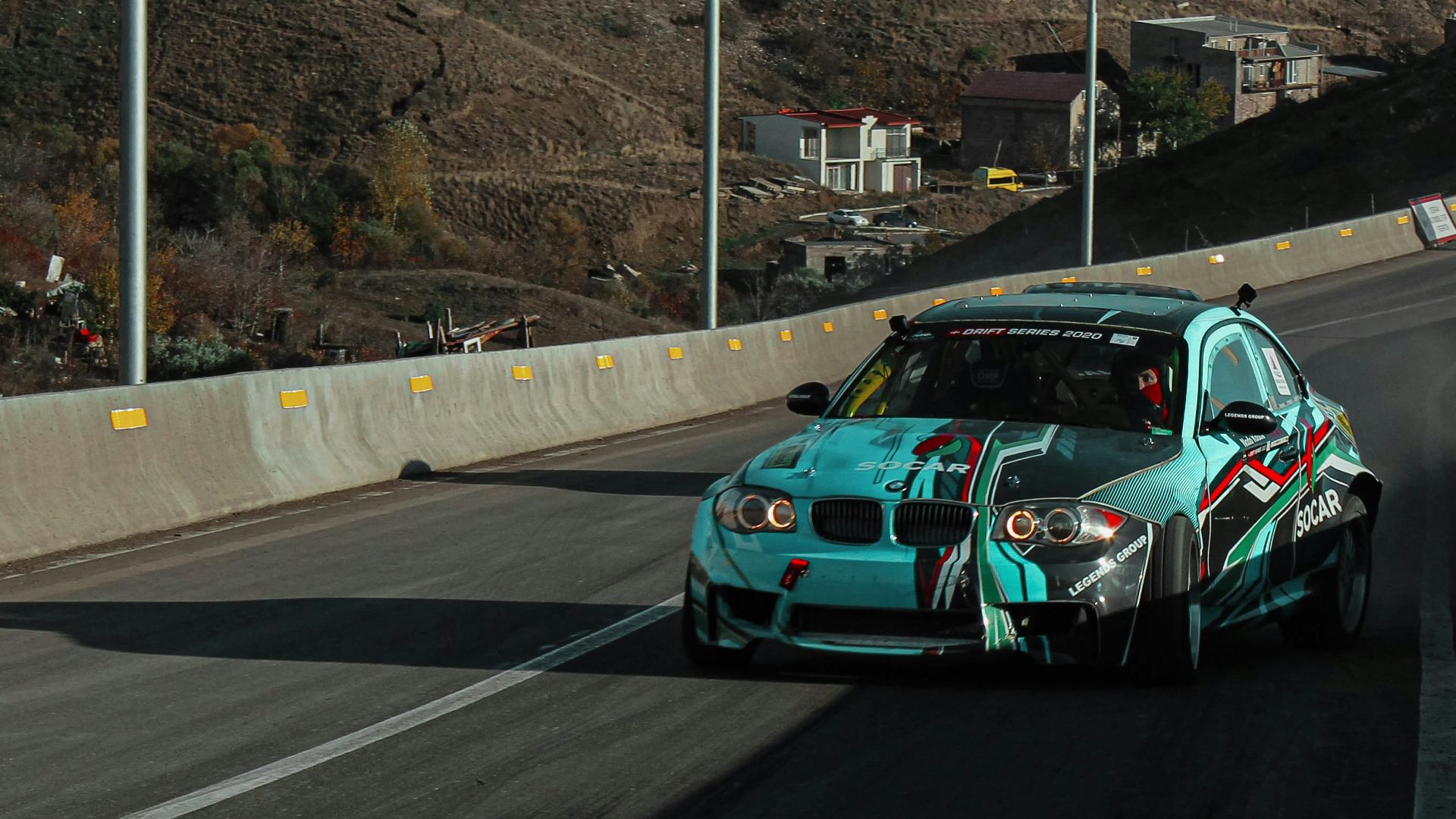 a blue car driving down a road next to a hillside
