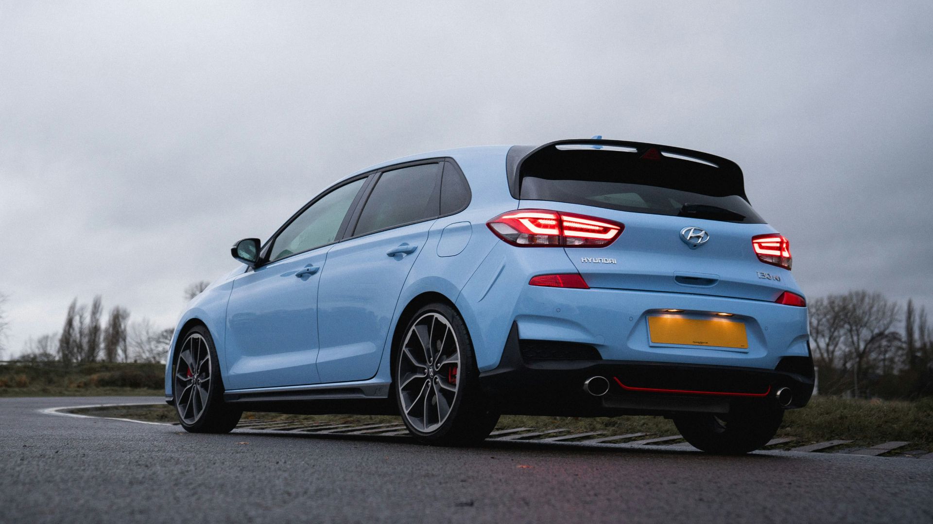 A light blue performance hatchback parked on a wet road.