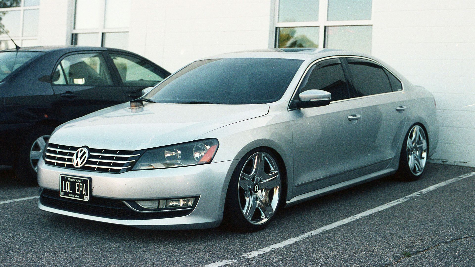 A silver car parked next to a black car in a parking lot