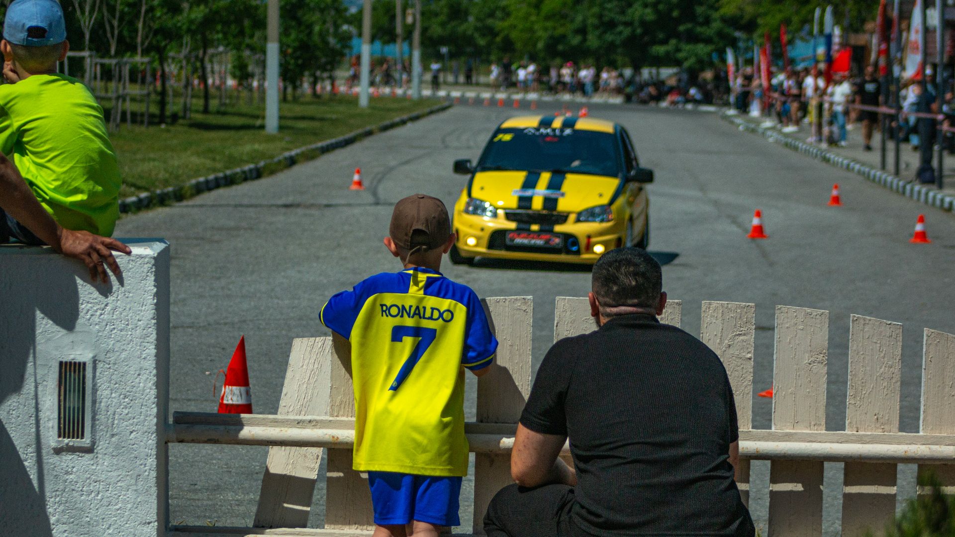 People watch a yellow car race on a track.