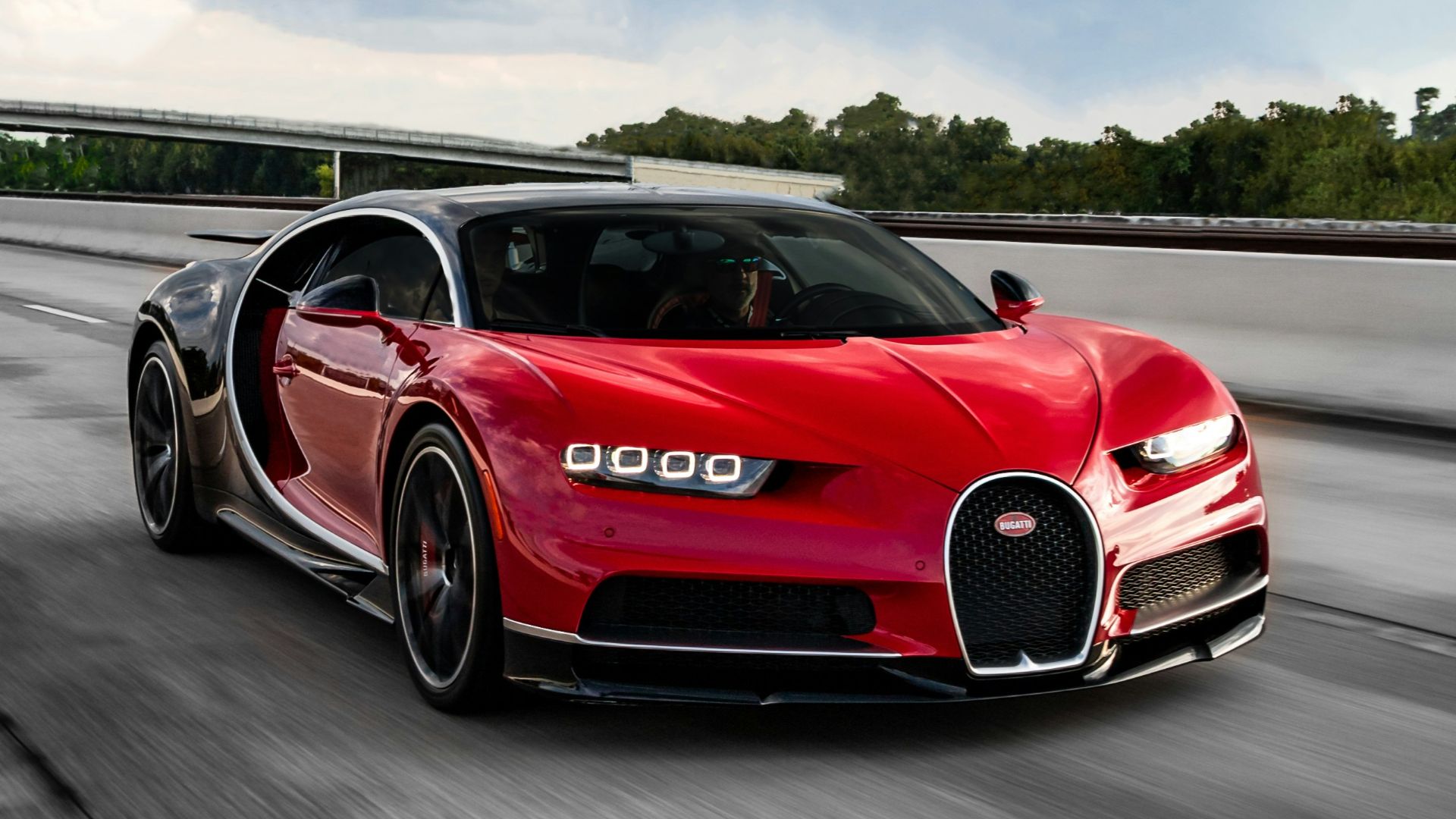 a red bugatti driving down a highway under a cloudy sky