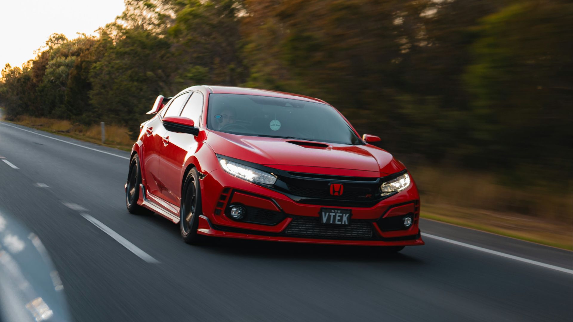 a red car driving down a road next to trees