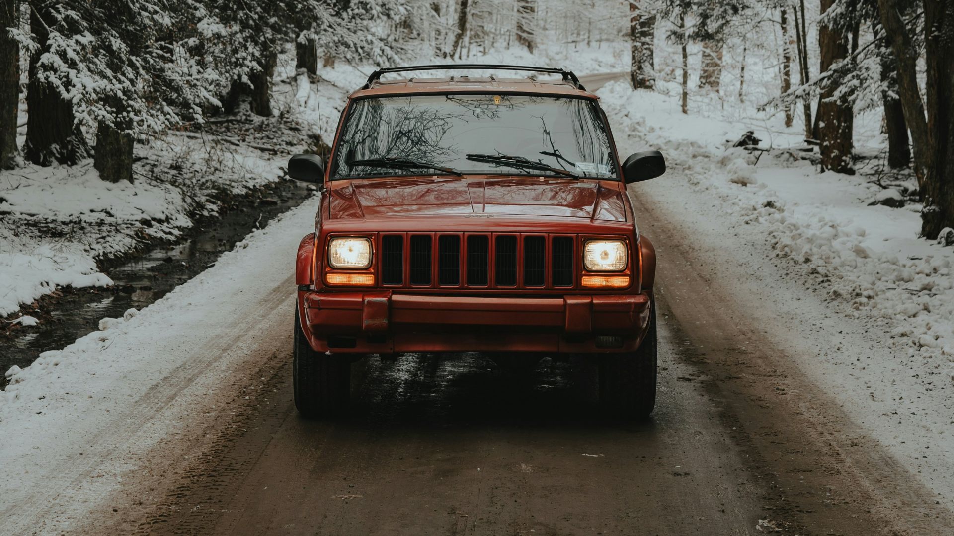 a red jeep driving down a snow covered road