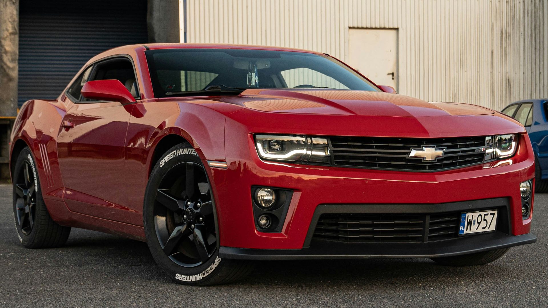 A red camaro is parked with two others.