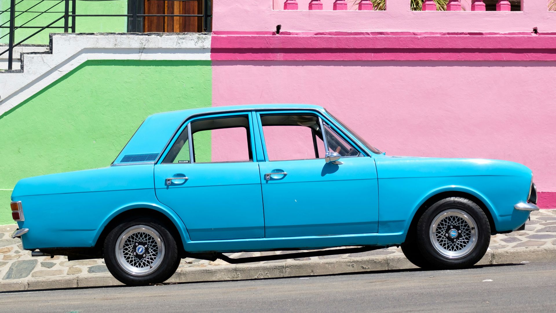 blue sedan parked beside pink and green house