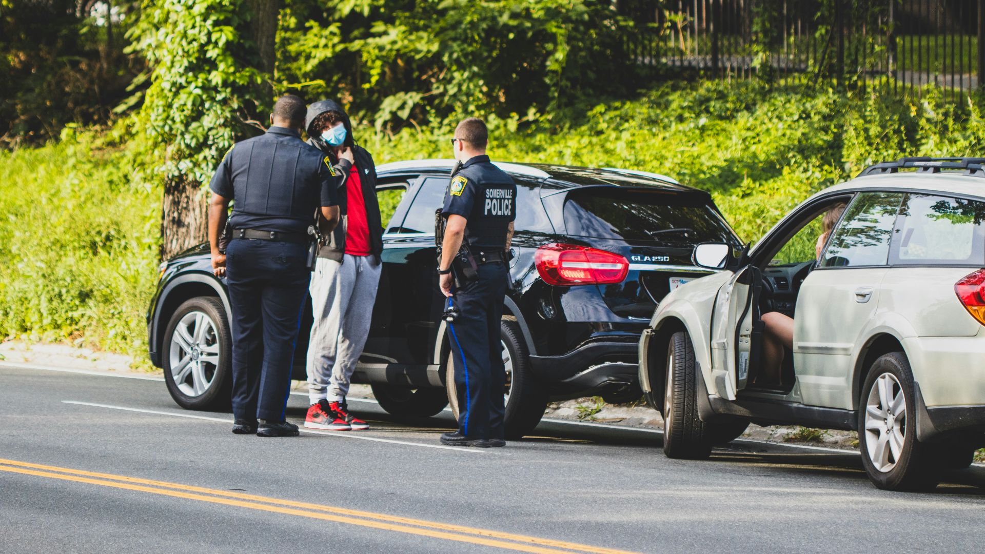 man in black t-shirt and black pants standing beside black suv during daytime