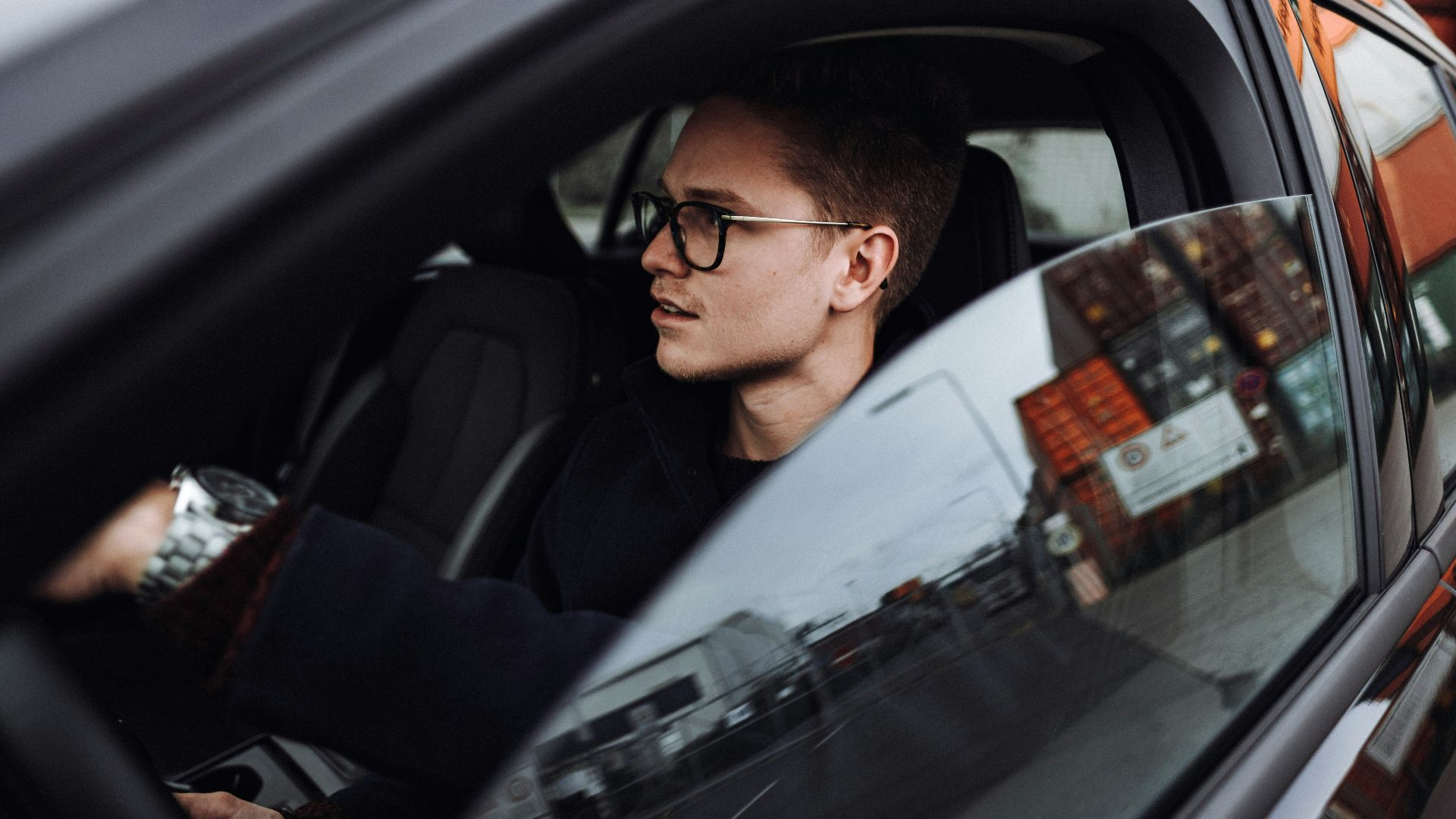 man in black jacket wearing eyeglasses sitting inside car
