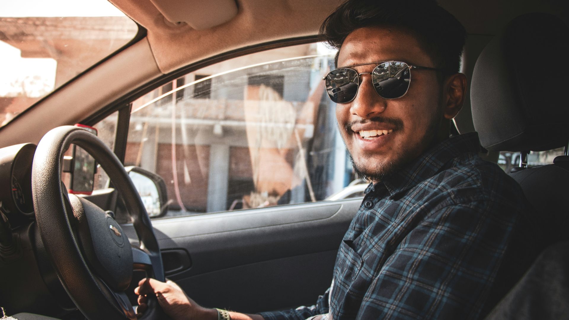 man in black and white plaid dress shirt wearing black sunglasses driving car