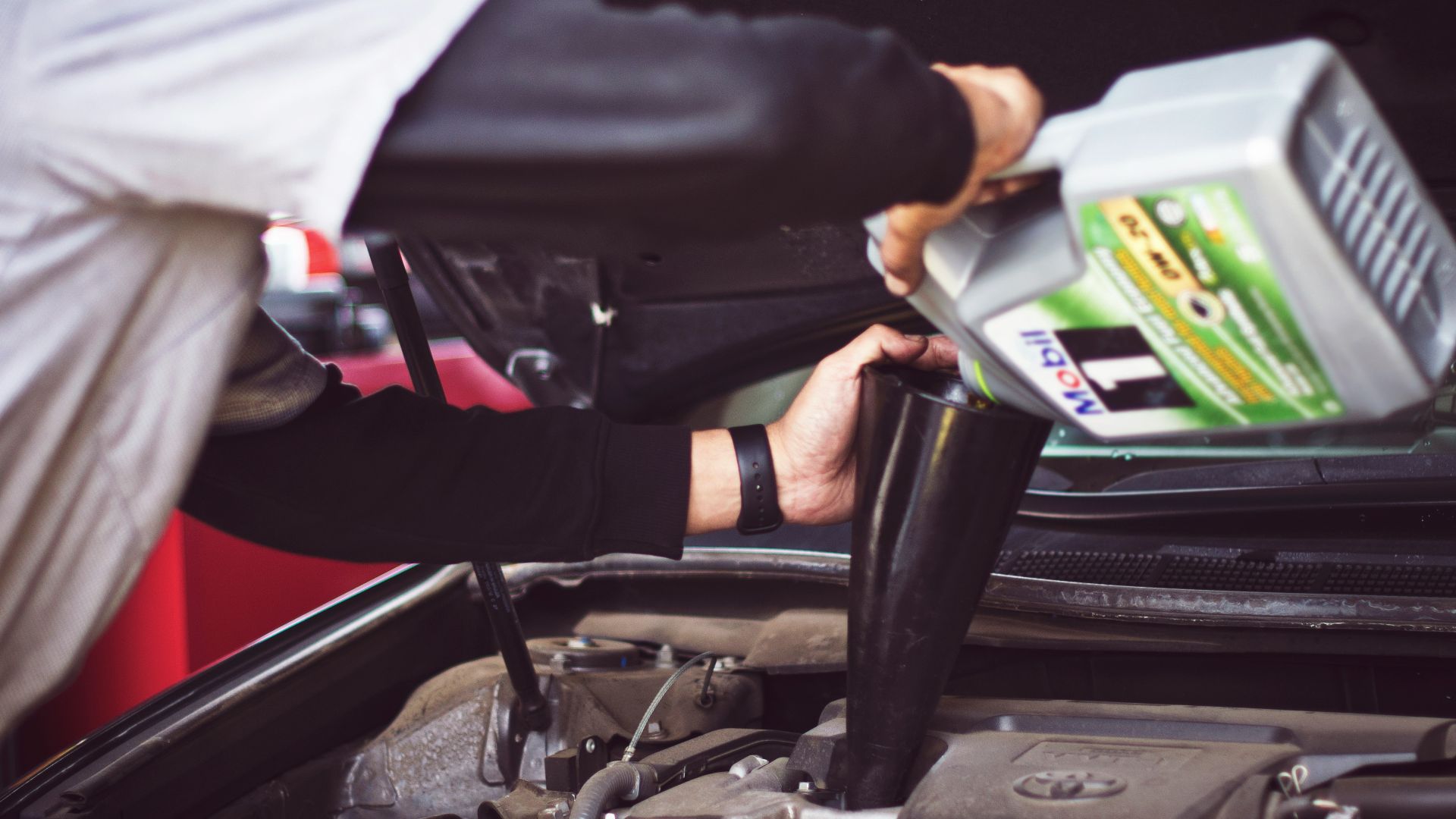 man refilling motor oil on car engine bay