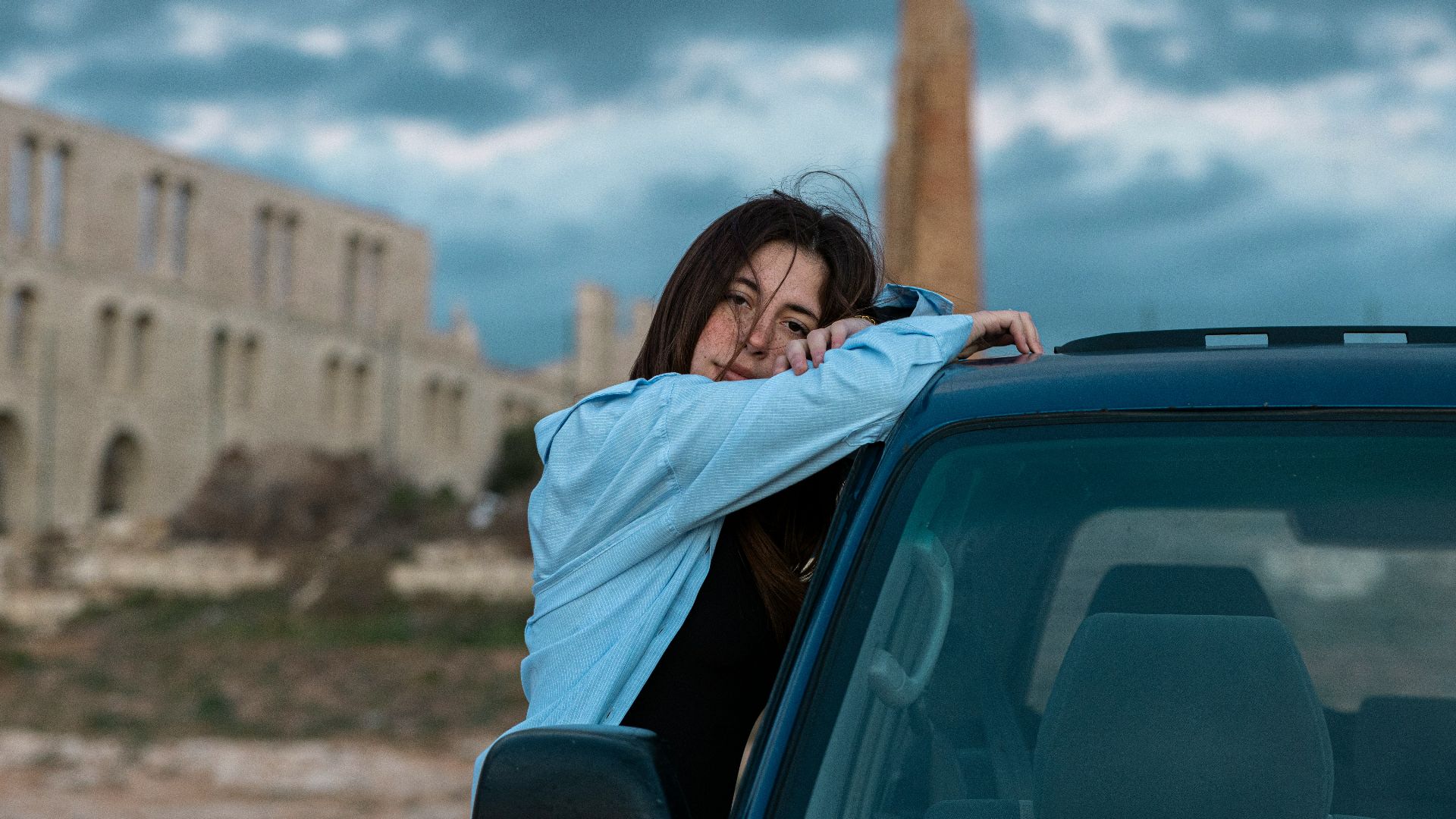 A woman leaning on the hood of a car