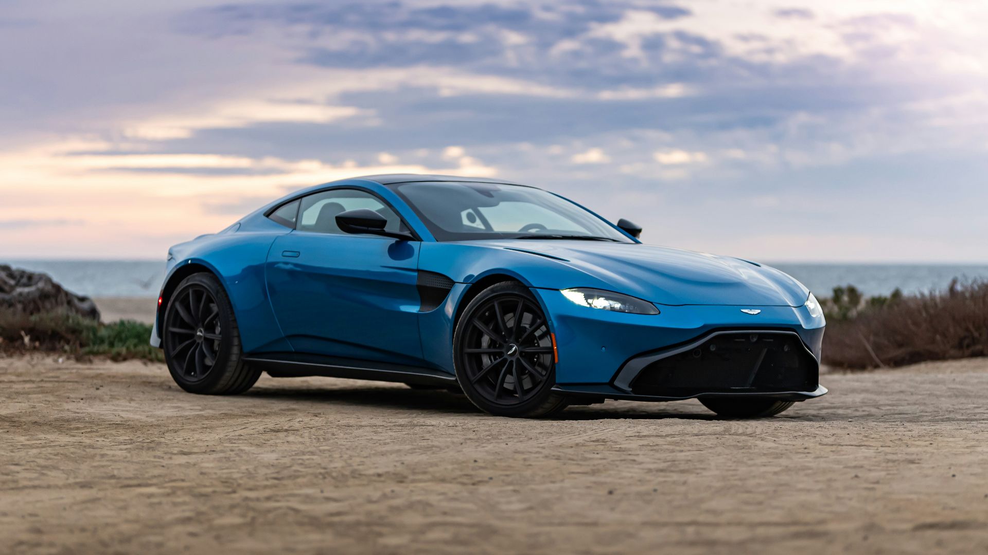 blue porsche 911 on brown sand under white clouds during daytime