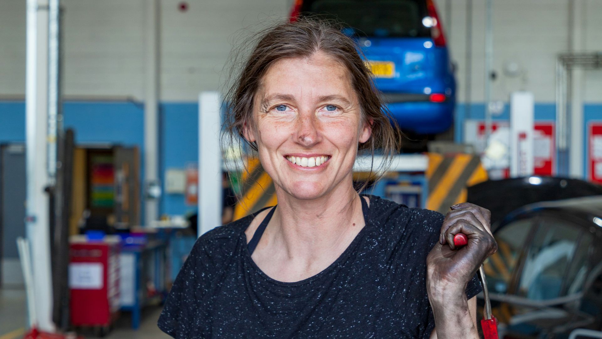 a woman holding a wrench in a garage