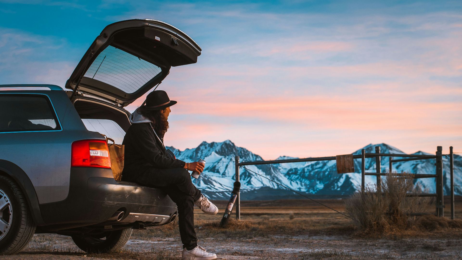 man sitting on car's tail looking at ranch