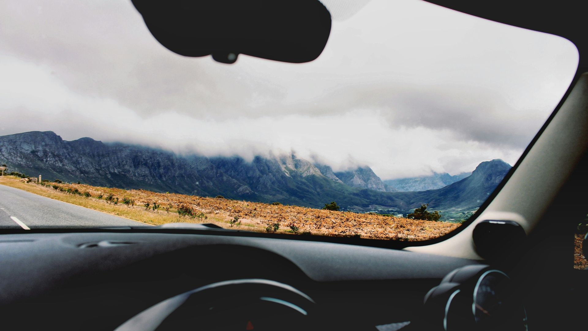 photo of car on road beside brown open field during cloudy daytime