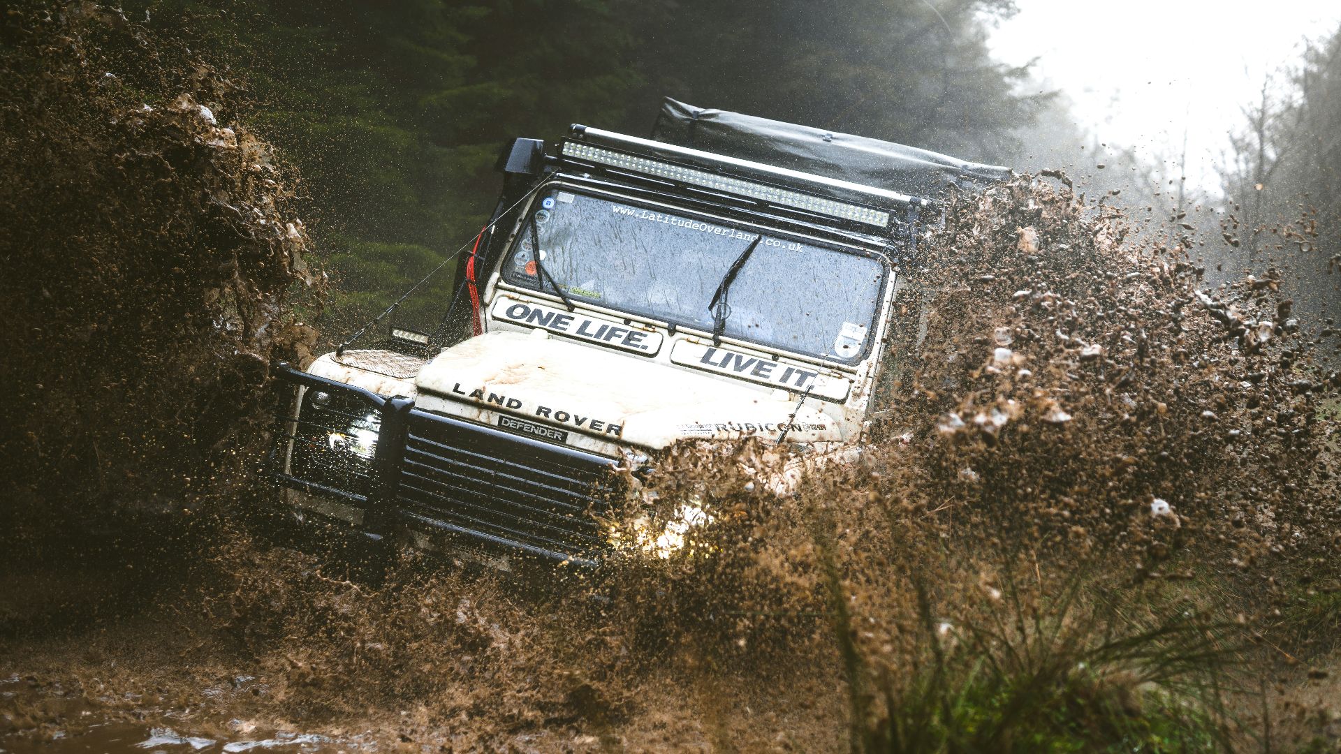 An off-road vehicle splashes through muddy water.