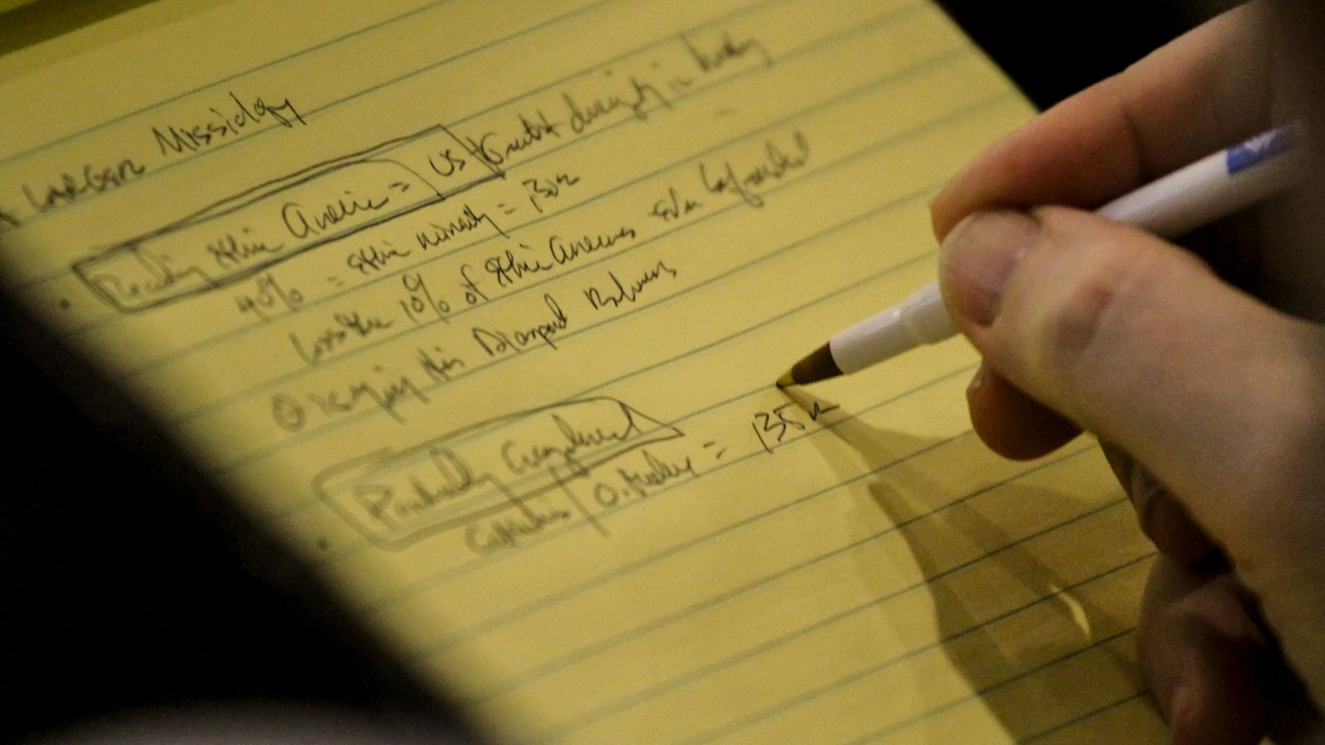 person holding white and black pen writing on yellow paper