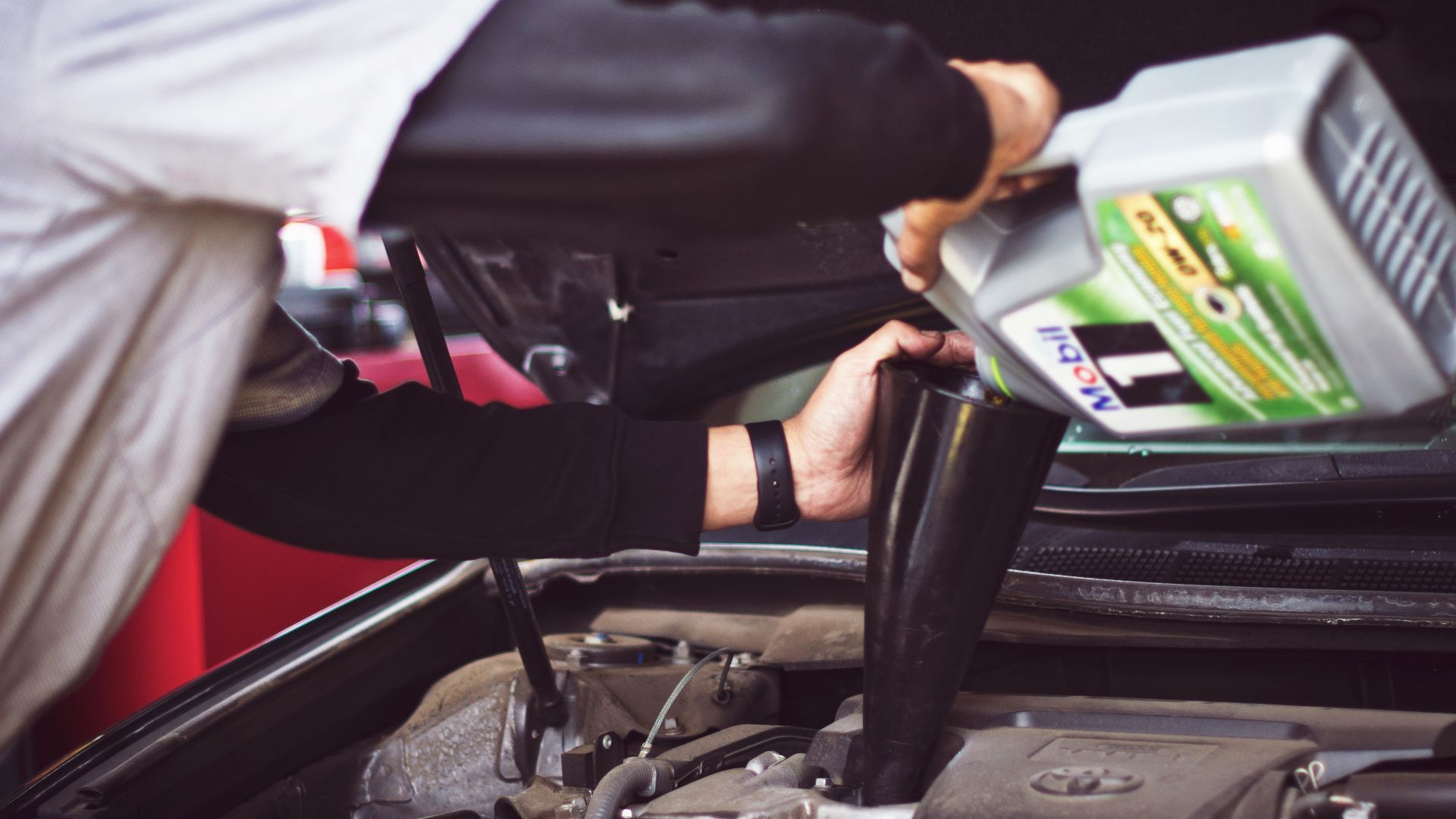 man refilling motor oil on car engine bay