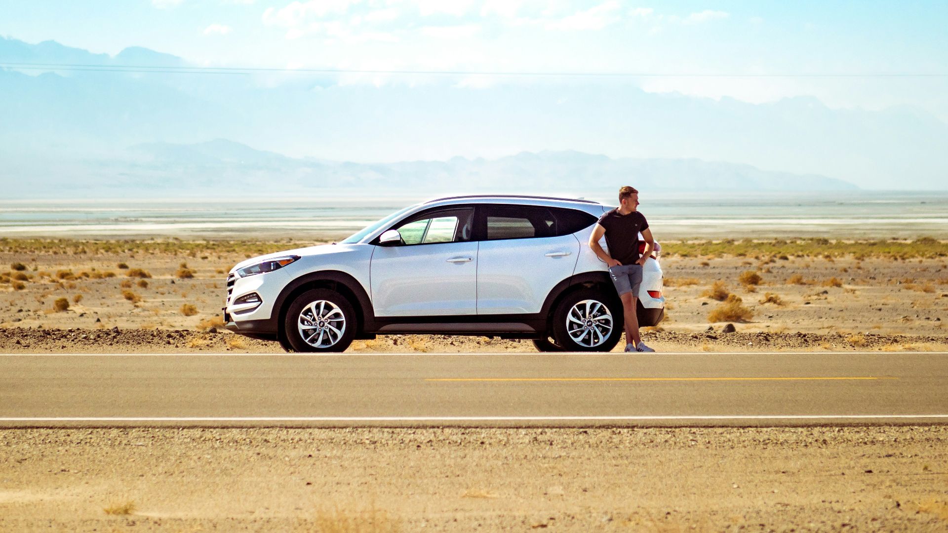 man standing beside white SUV near concrete road under blue sky at daytime