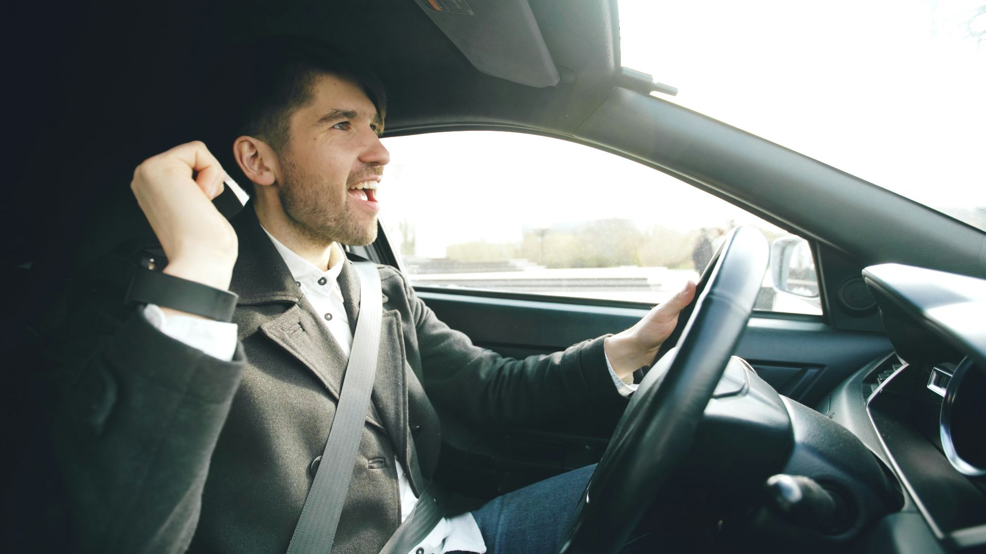 Man singing and driving a car enthusiastically.