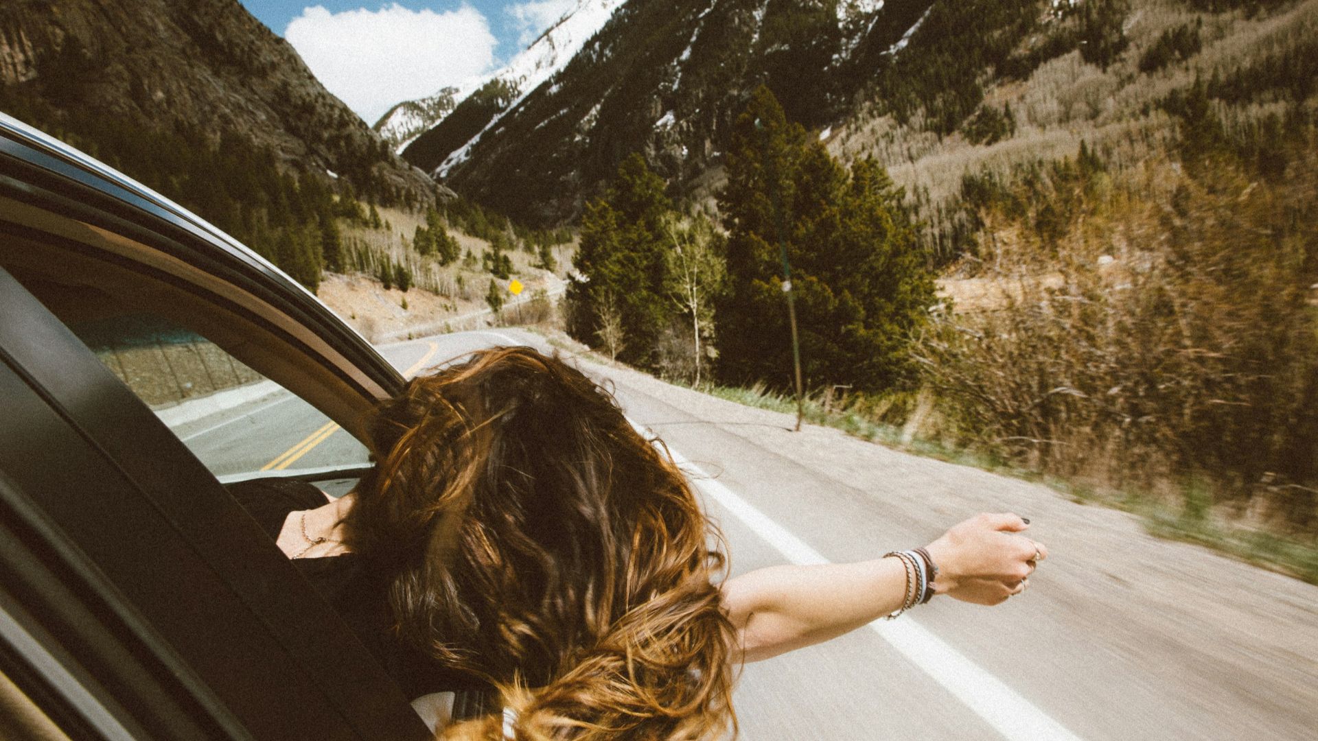woman riding on vehicle putting her head and right arm outside the window while travelling the road