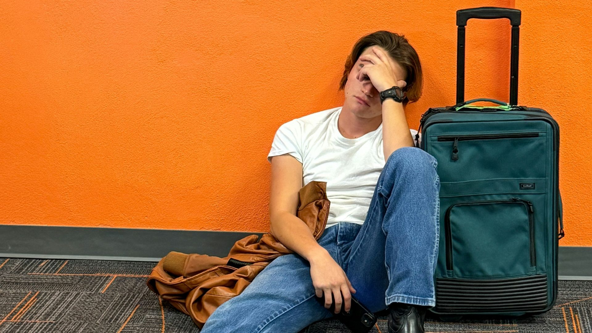 Man sitting on floor with luggage, looking tired.
