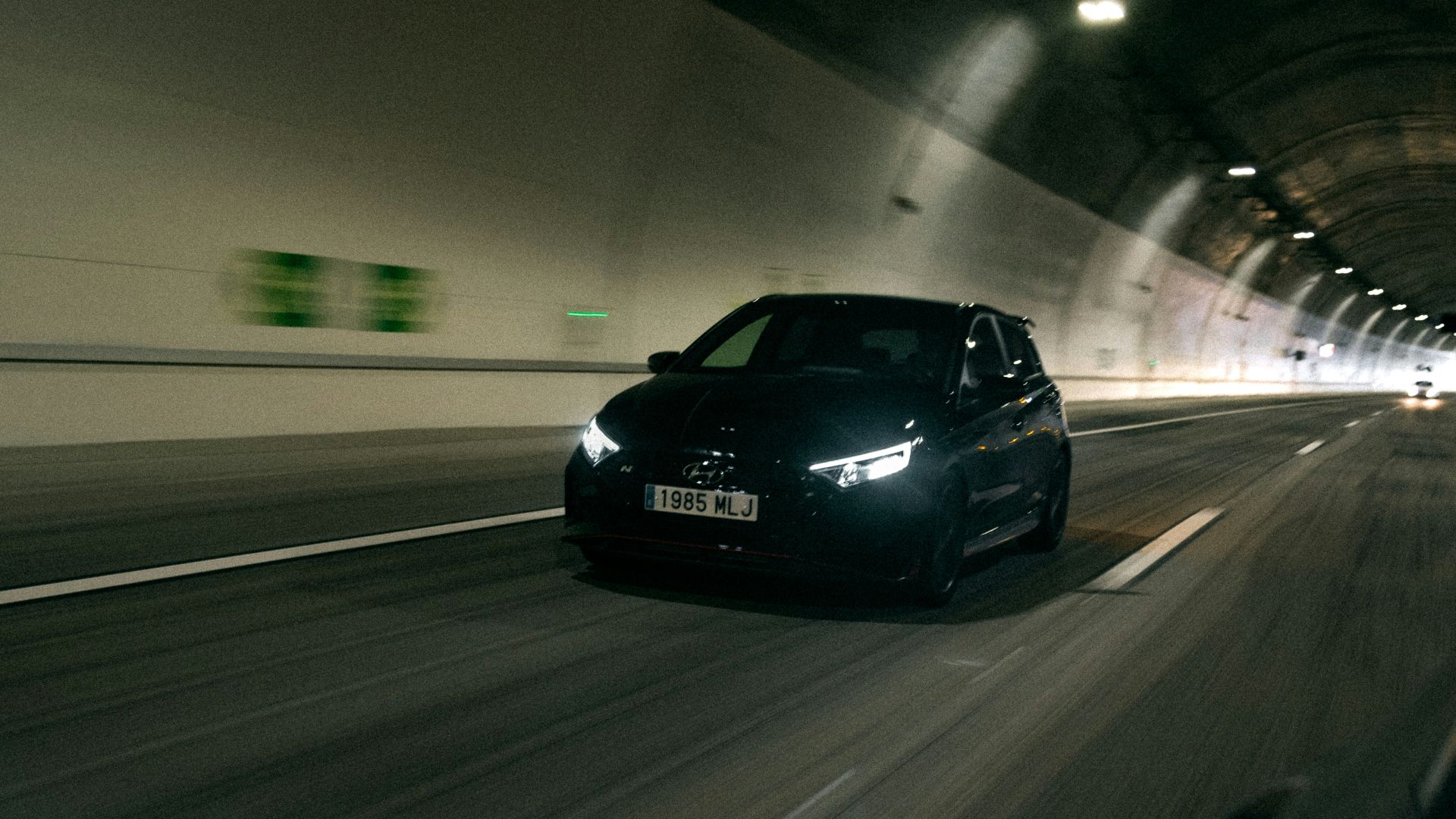 Black car driving through a brightly lit tunnel.