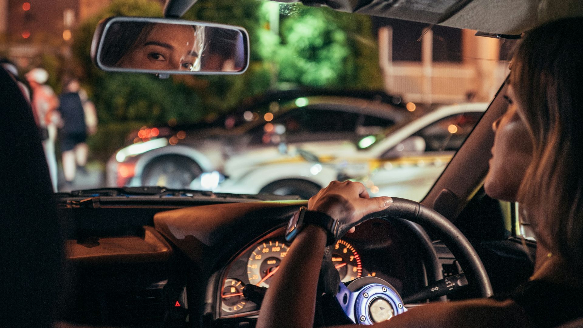 Woman driving car at night with city lights reflection