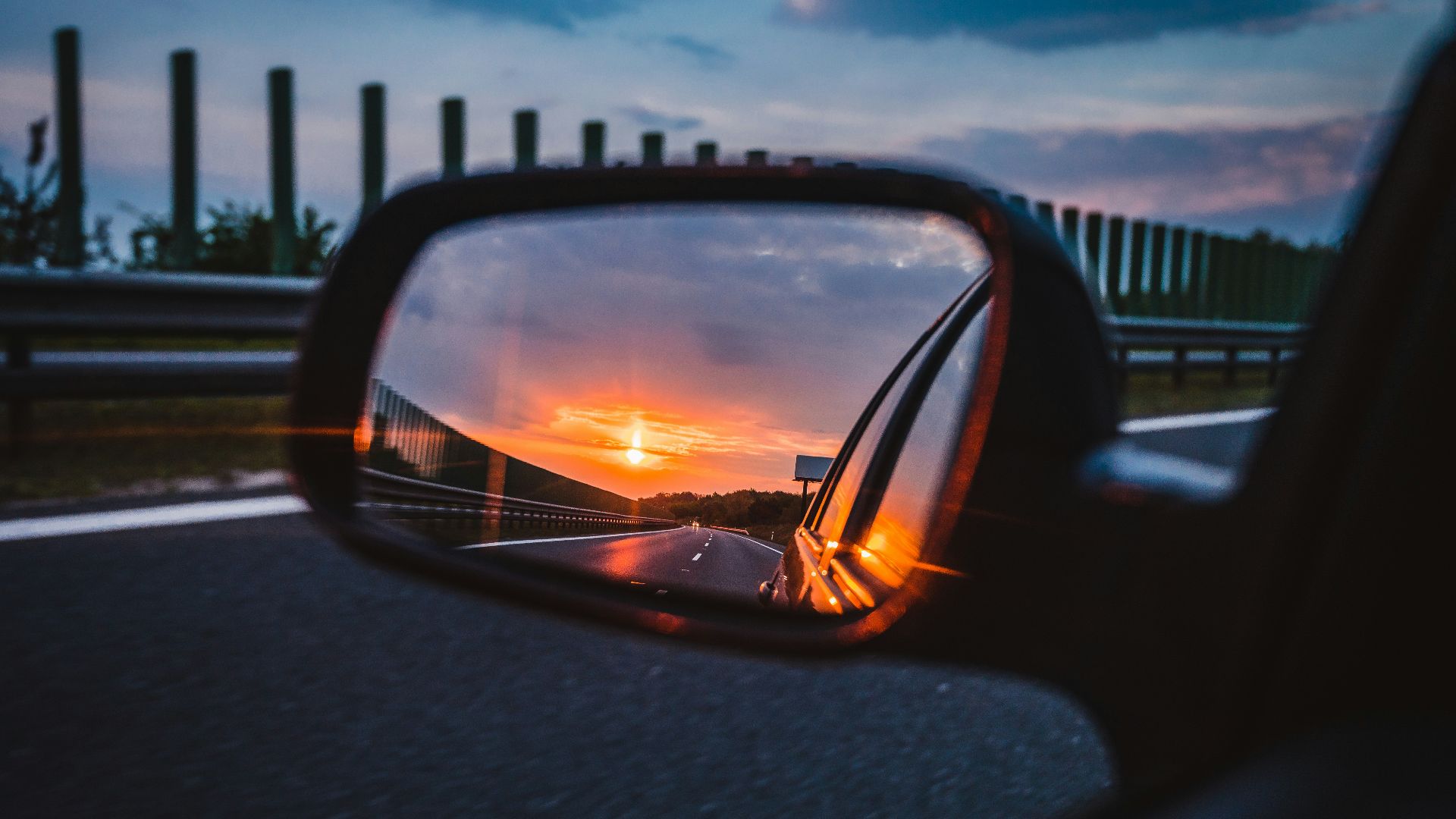 a rear view mirror reflecting a sunset in the side view mirror