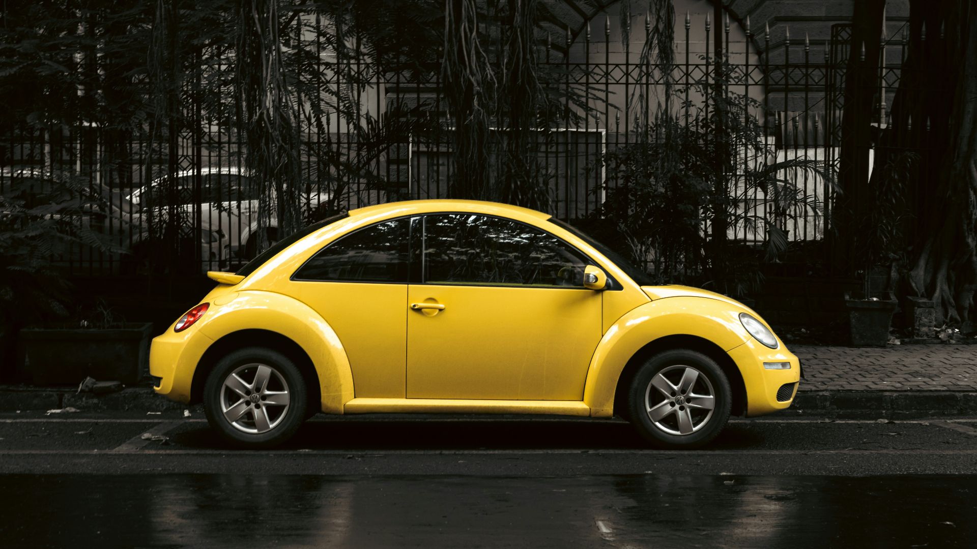 A bright yellow volkswagen beetle parks on the street.