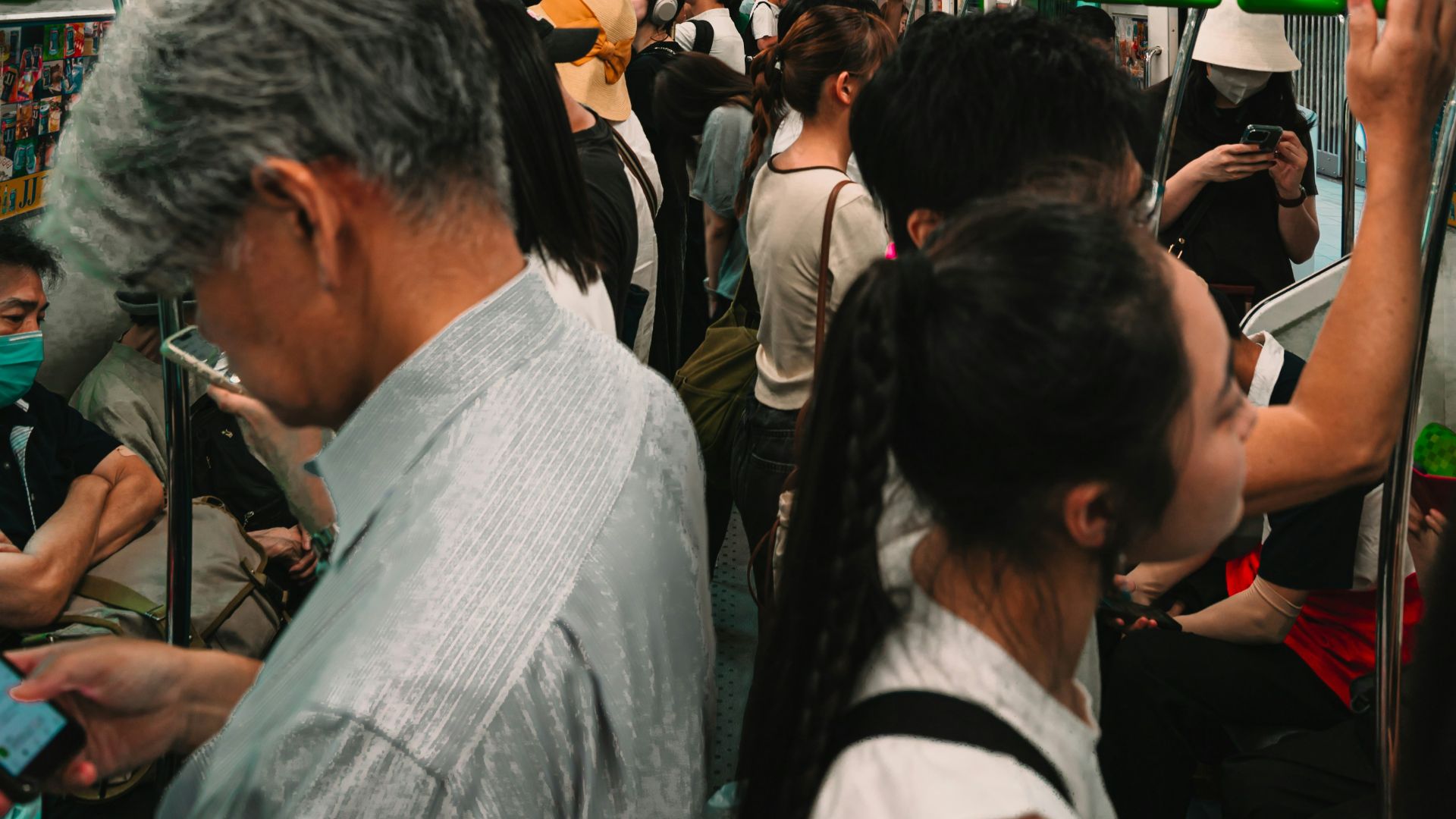 Crowded subway train with passengers holding green handles.