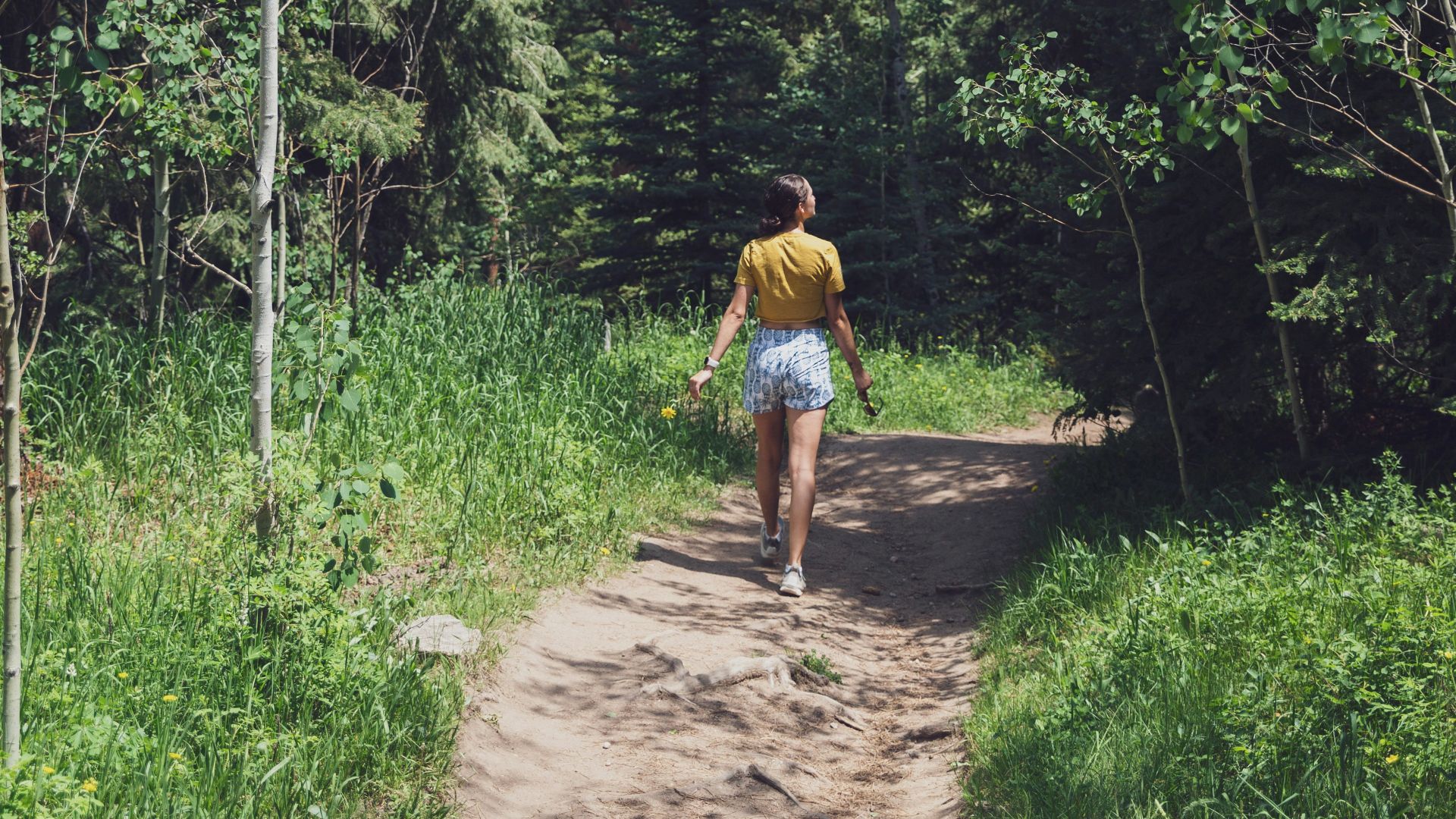 man in yellow t-shirt and brown shorts walking on pathway surrounded by green trees during