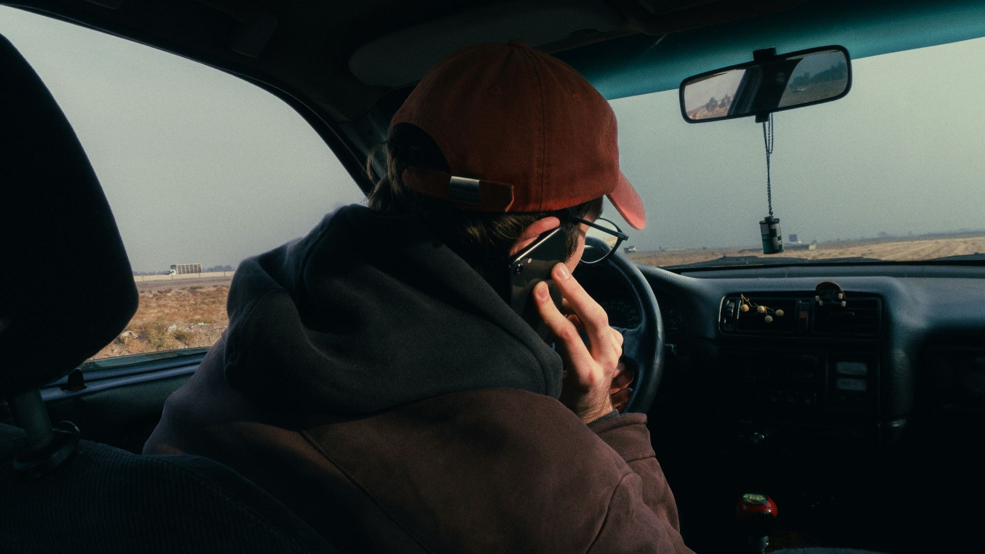 Person in car wearing a hat and glasses.