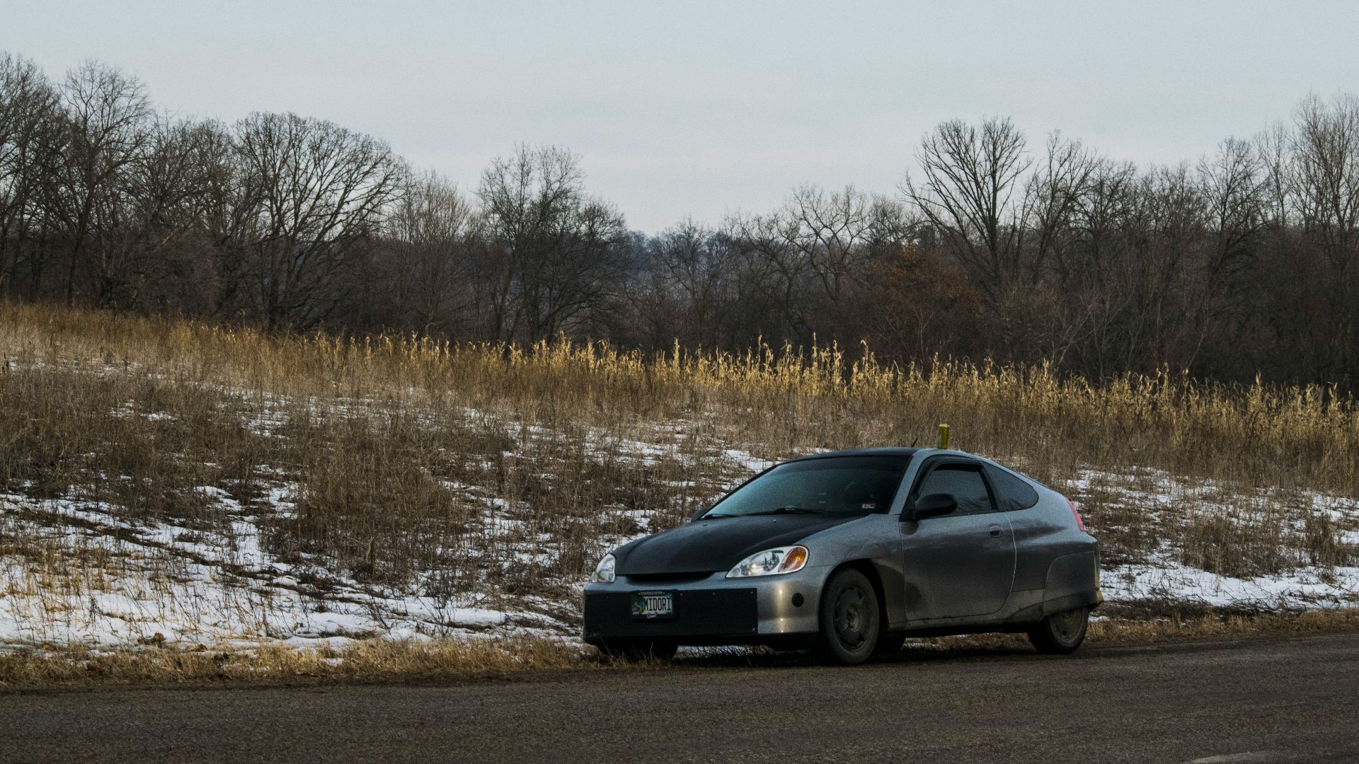 A gray car is parked near a snowy roadside.