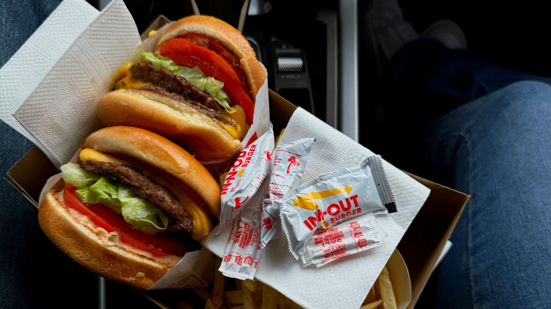 Two burgers, fries, and a drink in a car.