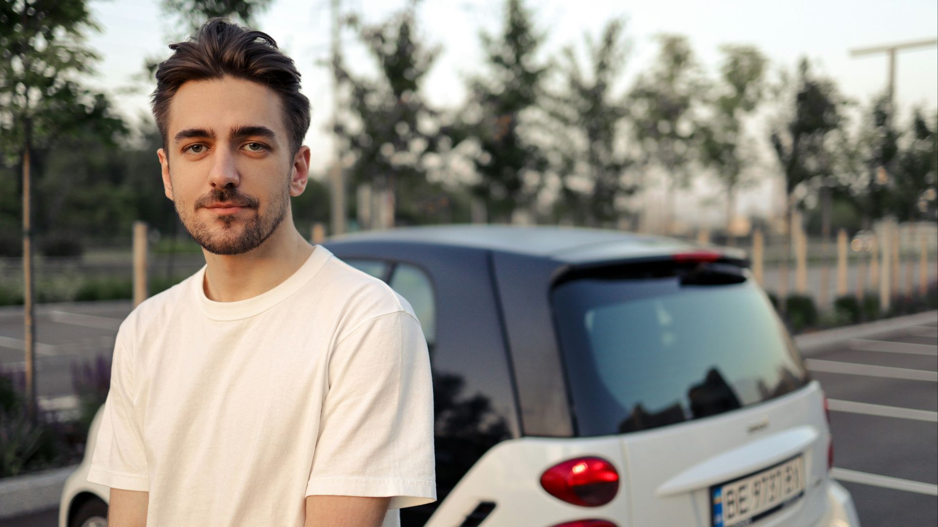 man in white crew neck t-shirt standing beside white car during daytime