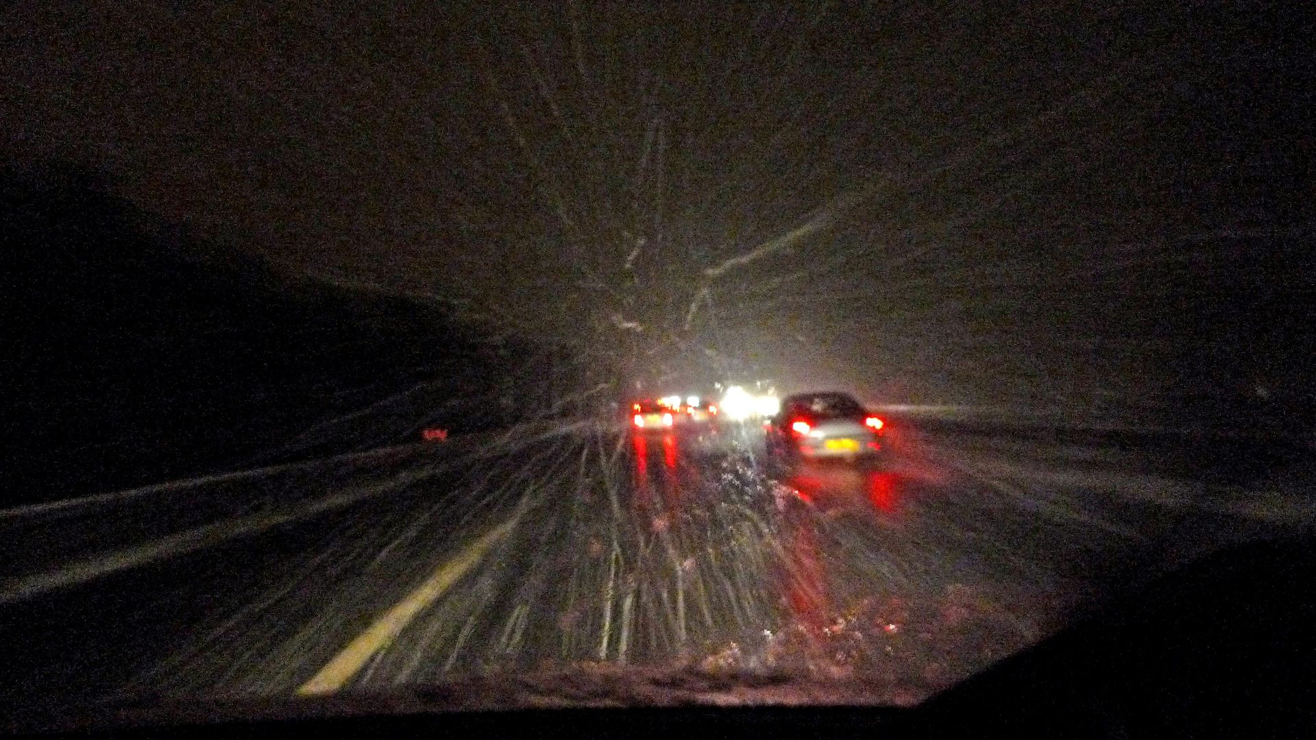 Driving on a wet road at night with headlights.