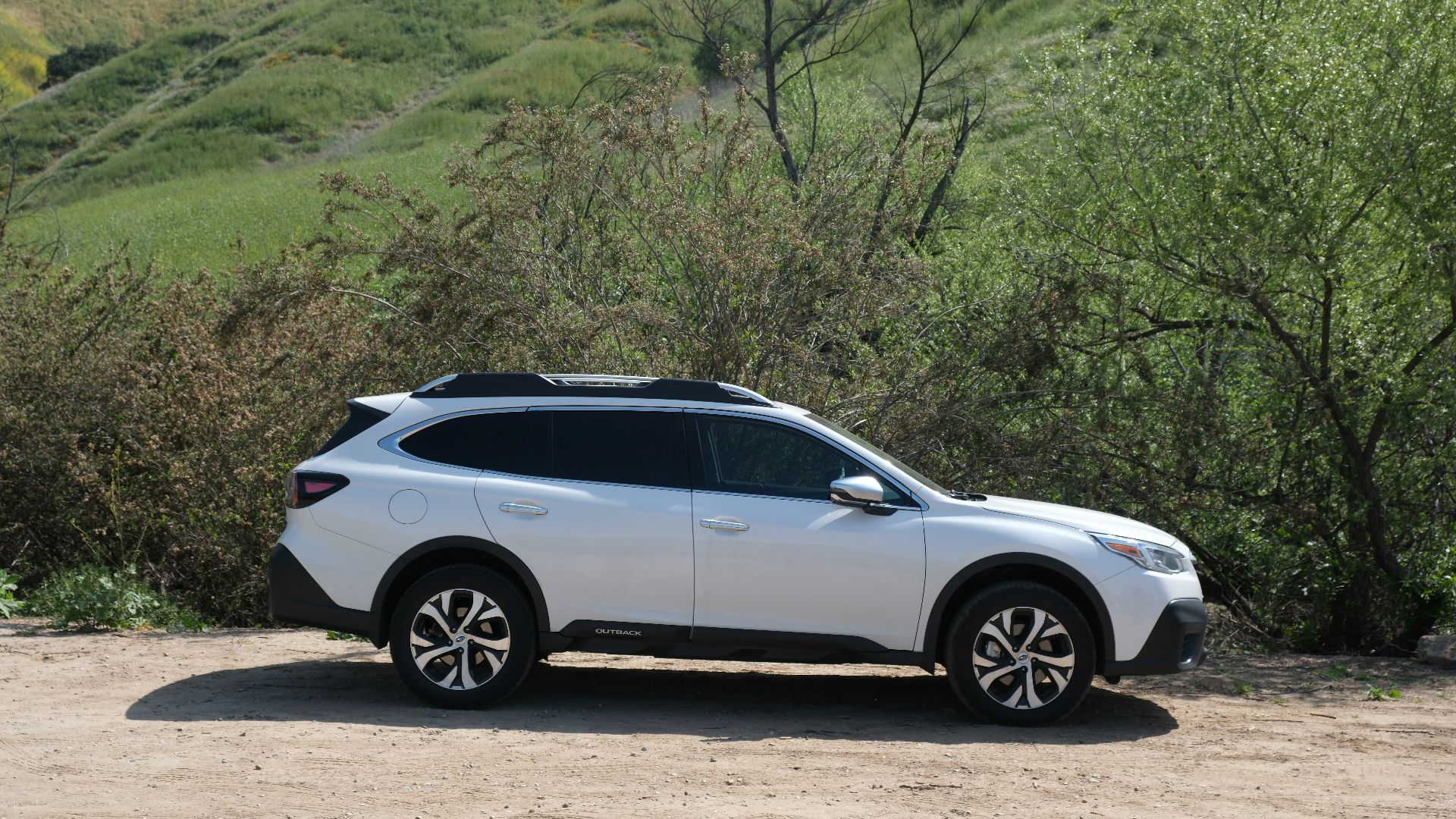 a white car parked in front of a lush green hillside