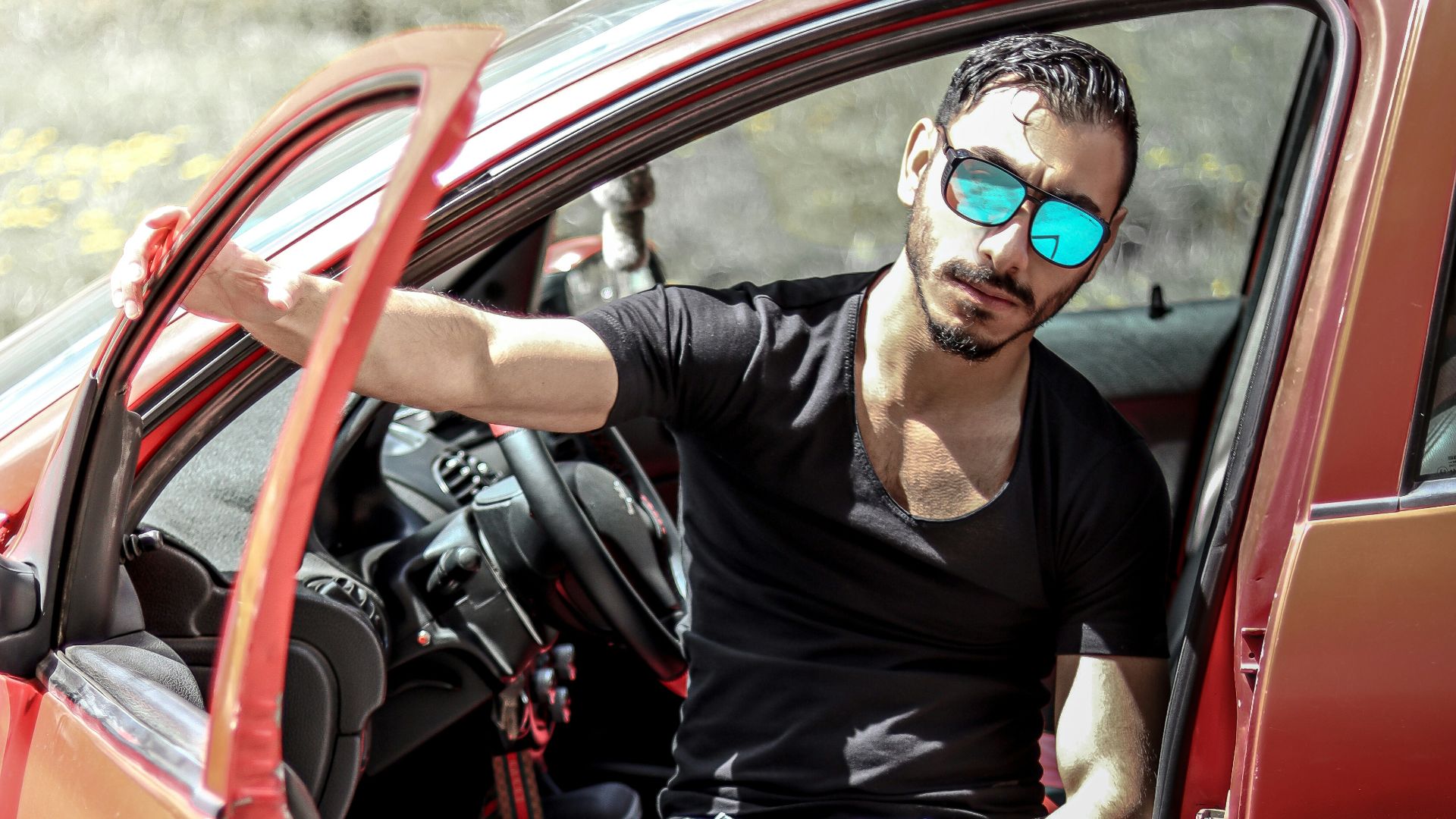 A stylish man poses in a red car.