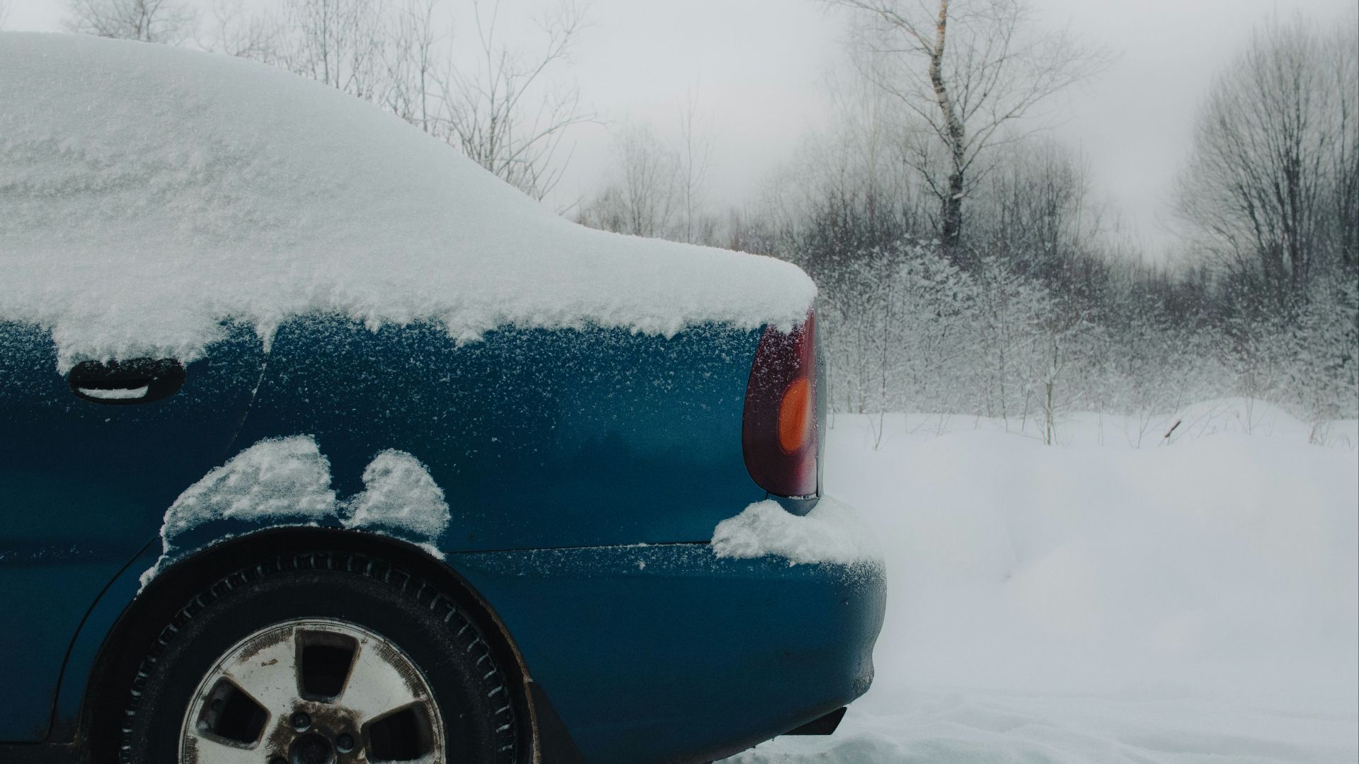 a blue car covered in snow on a snowy day