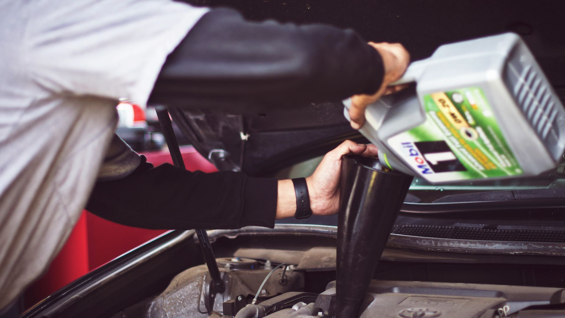 man refilling motor oil on car engine bay