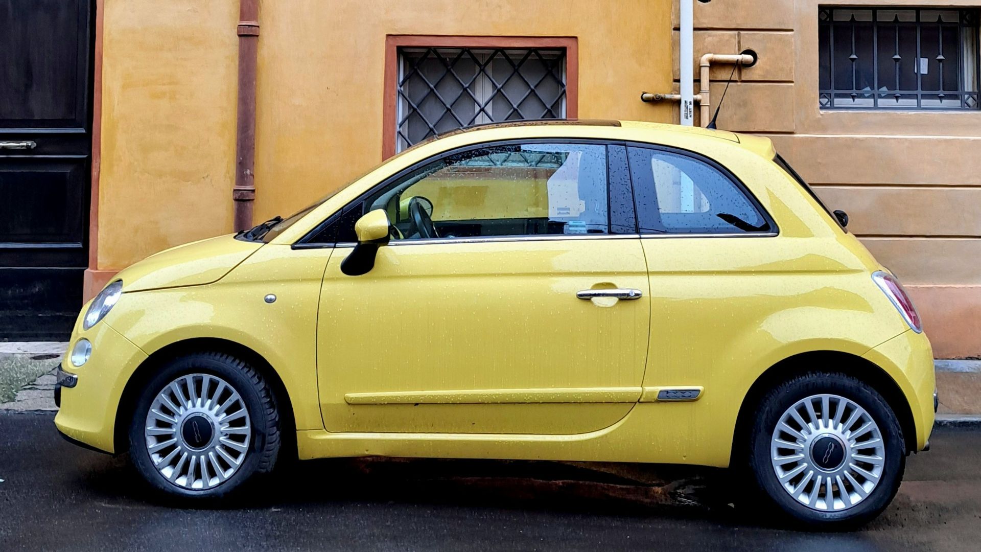A yellow fiat 500 parked on a wet street.