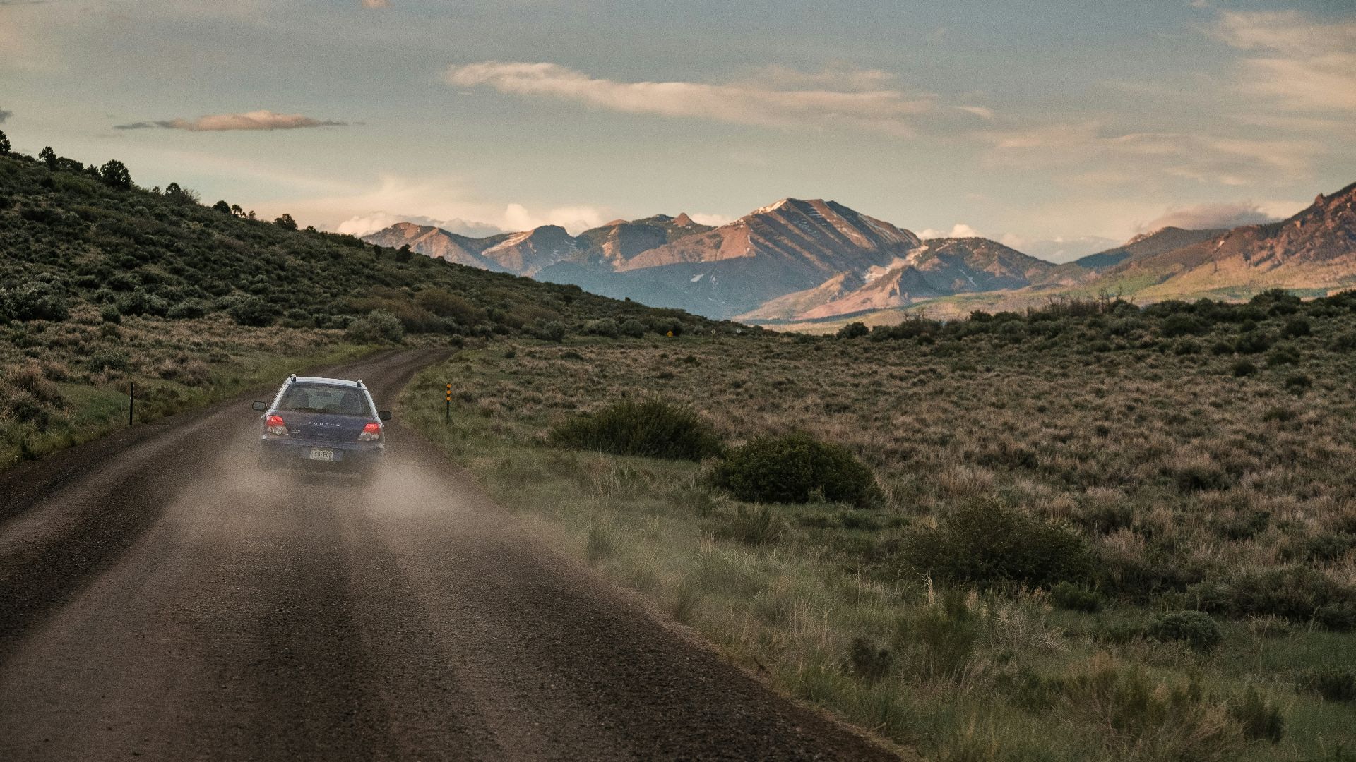 a car driving down a dirt road with mountains in the background