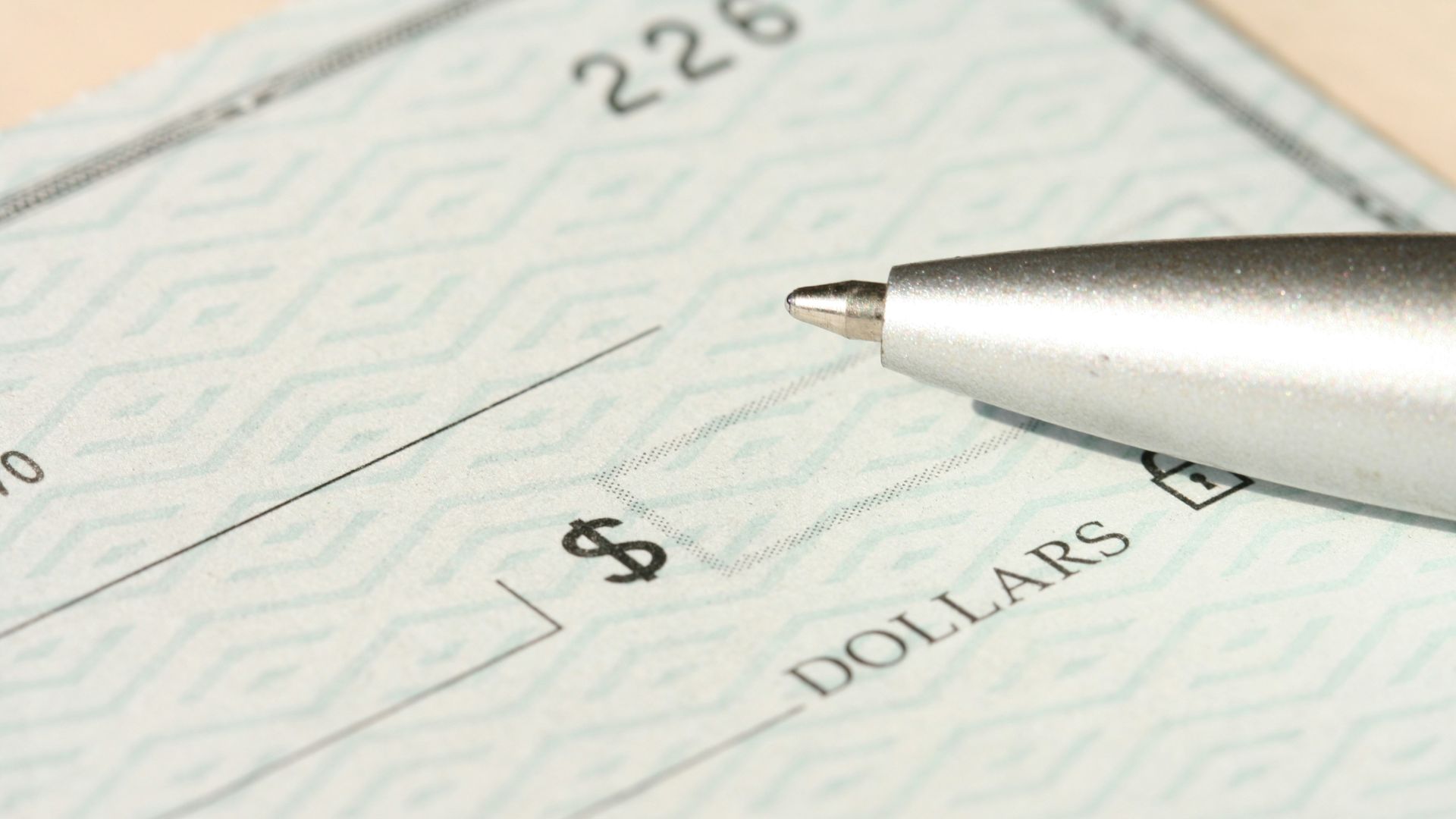 A pen rests on a check near the dollars line.