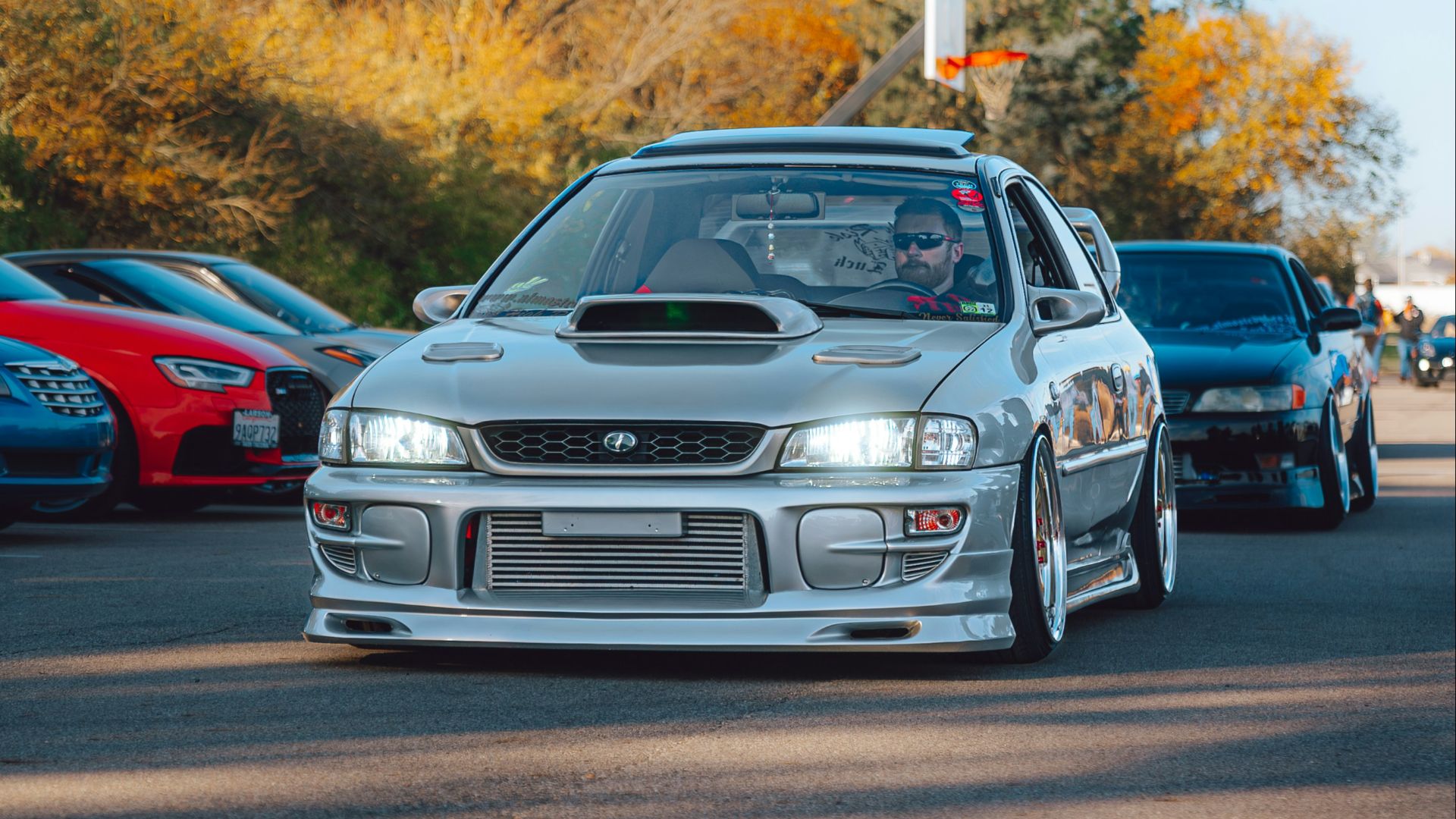 A silver car driving down a street next to a forest